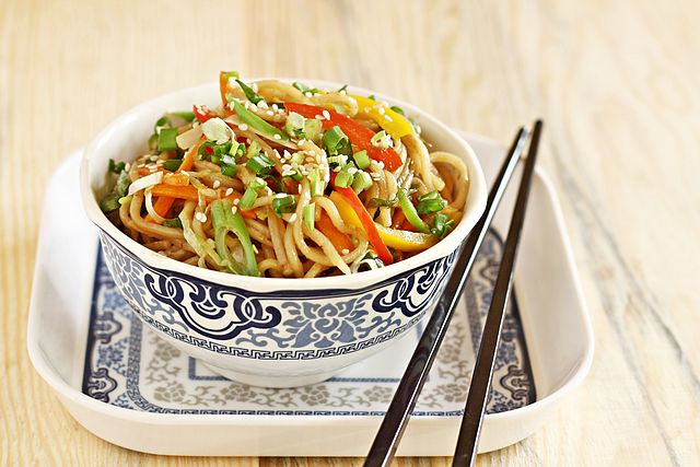 a bowl of hakka noodles cooked with various vegetables and topped with sesame seeds